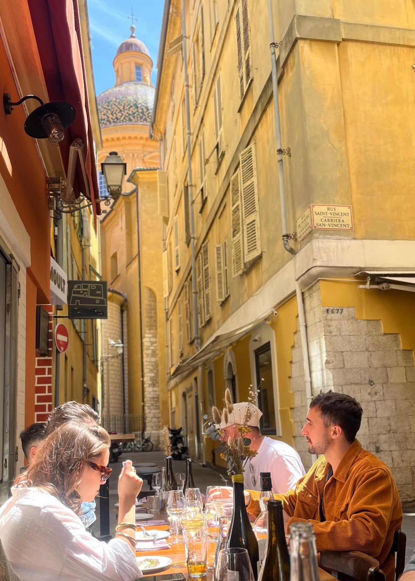 La ruelle du Vieux Nice devant Moult, tables dressées et coupole de la cathédrale Sainte-Réparate